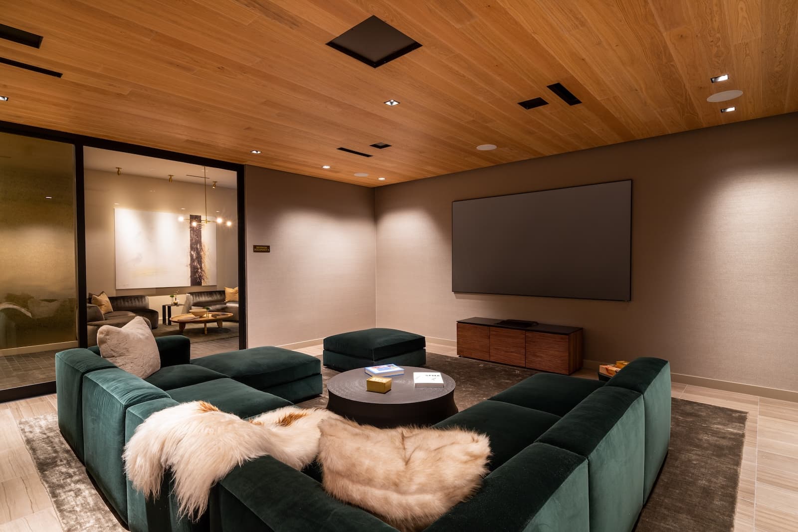 Resident screening room with a large screen, upholstered sectional seating, low coffee table, and warm wood ceiling.