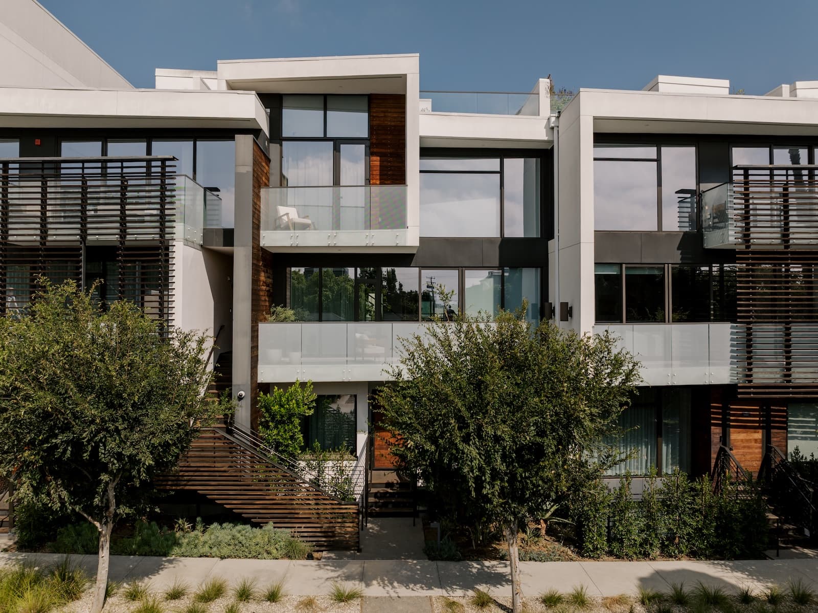 Modern luxury apartment building with glass balconies, clean concrete lines, and landscaped greenery in a contemporary urban setting.