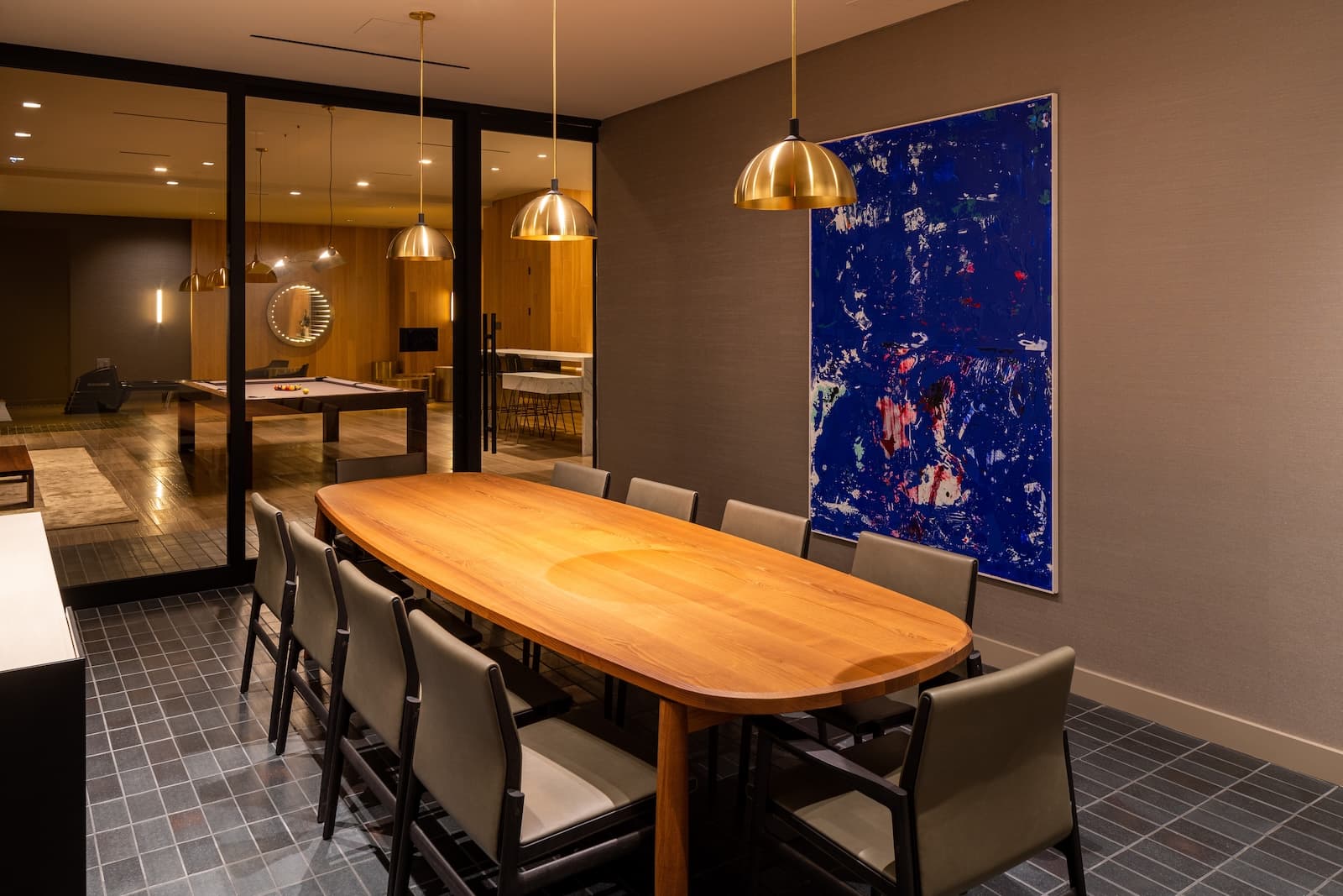 Private dining room amenity with a long wooden table surrounded by upholstered chairs, contemporary lighting overhead, and elegant decor.