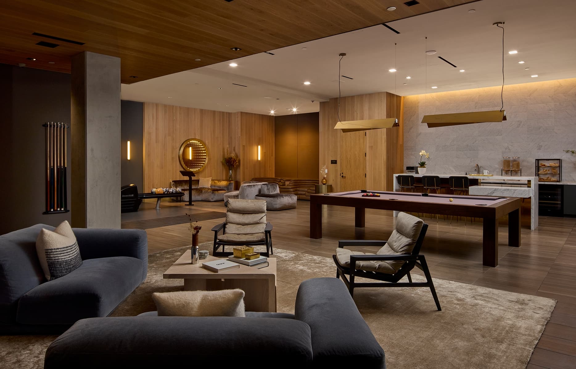 A spacious, double-height entertainment lounge at The Harland featuring a central pool table, contemporary seating areas, and high-end finishes including marble surfaces and dark metal accents. The space is designed for social gatherings and relaxation, with an open layout and curated furnishings.