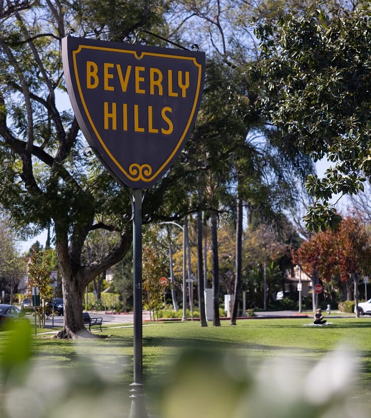 Beverly Hills sign surrounded by landscaped gardens and palm trees in a public park setting.