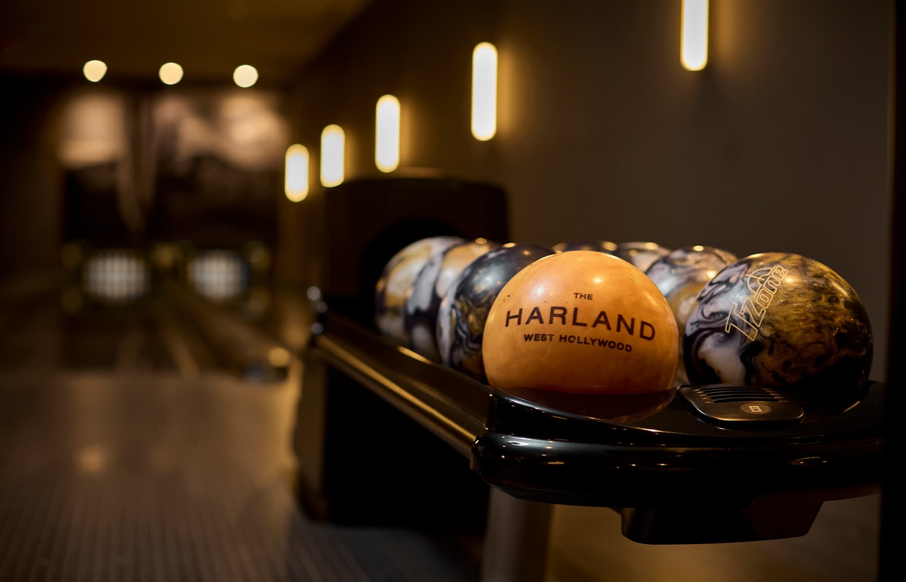 Close-up of bowling balls on rack in modern two-lane bowling alley with upscale finishes.